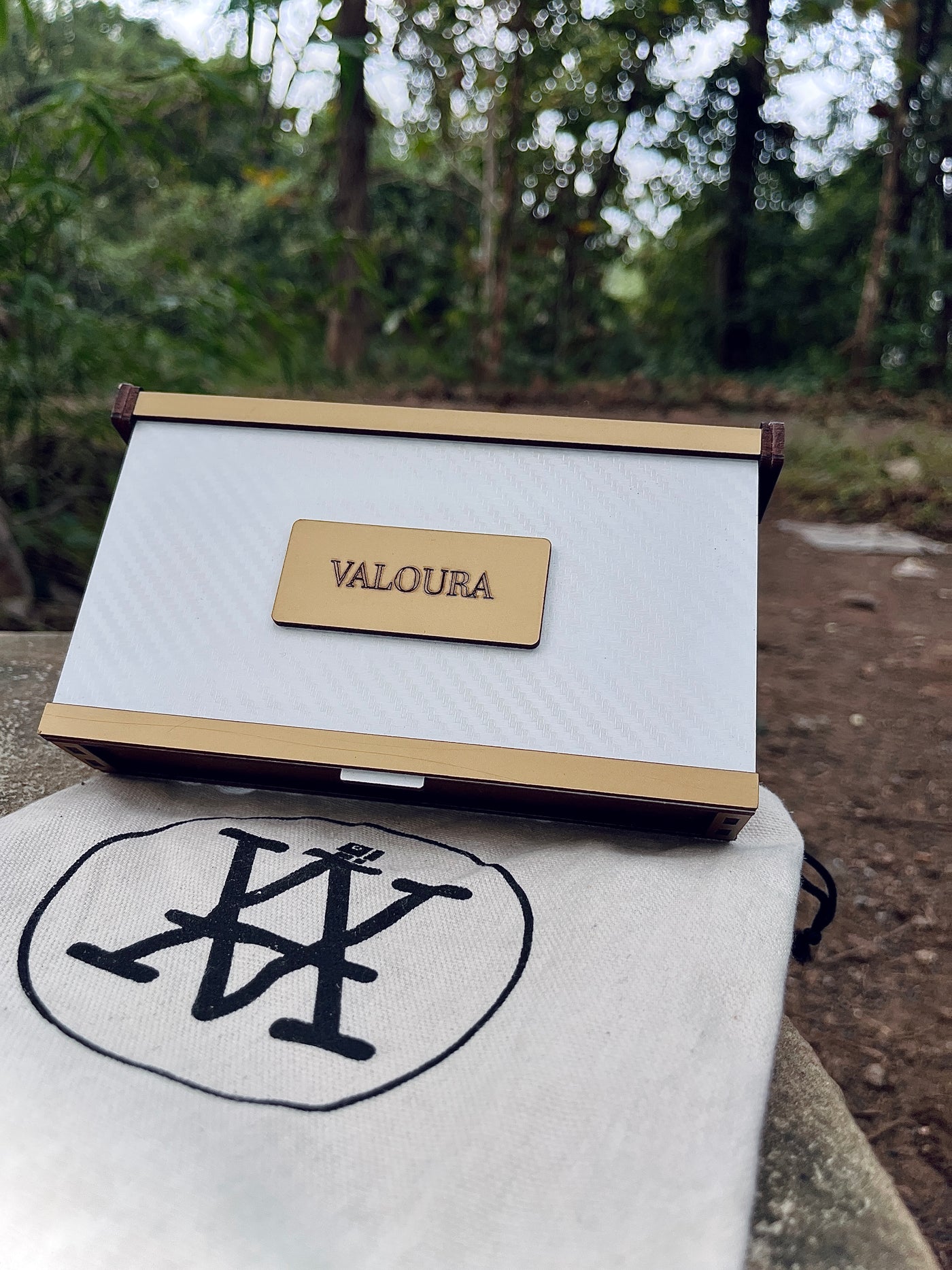 White and gold box with 'VALOURA' branding on a white surface outdoors in a forest scenery