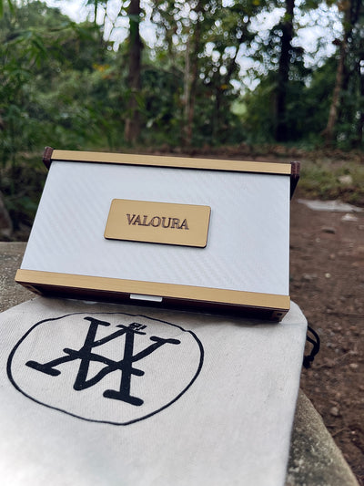 White and gold box with 'VALOURA' branding on a white surface outdoors in a forest scenery