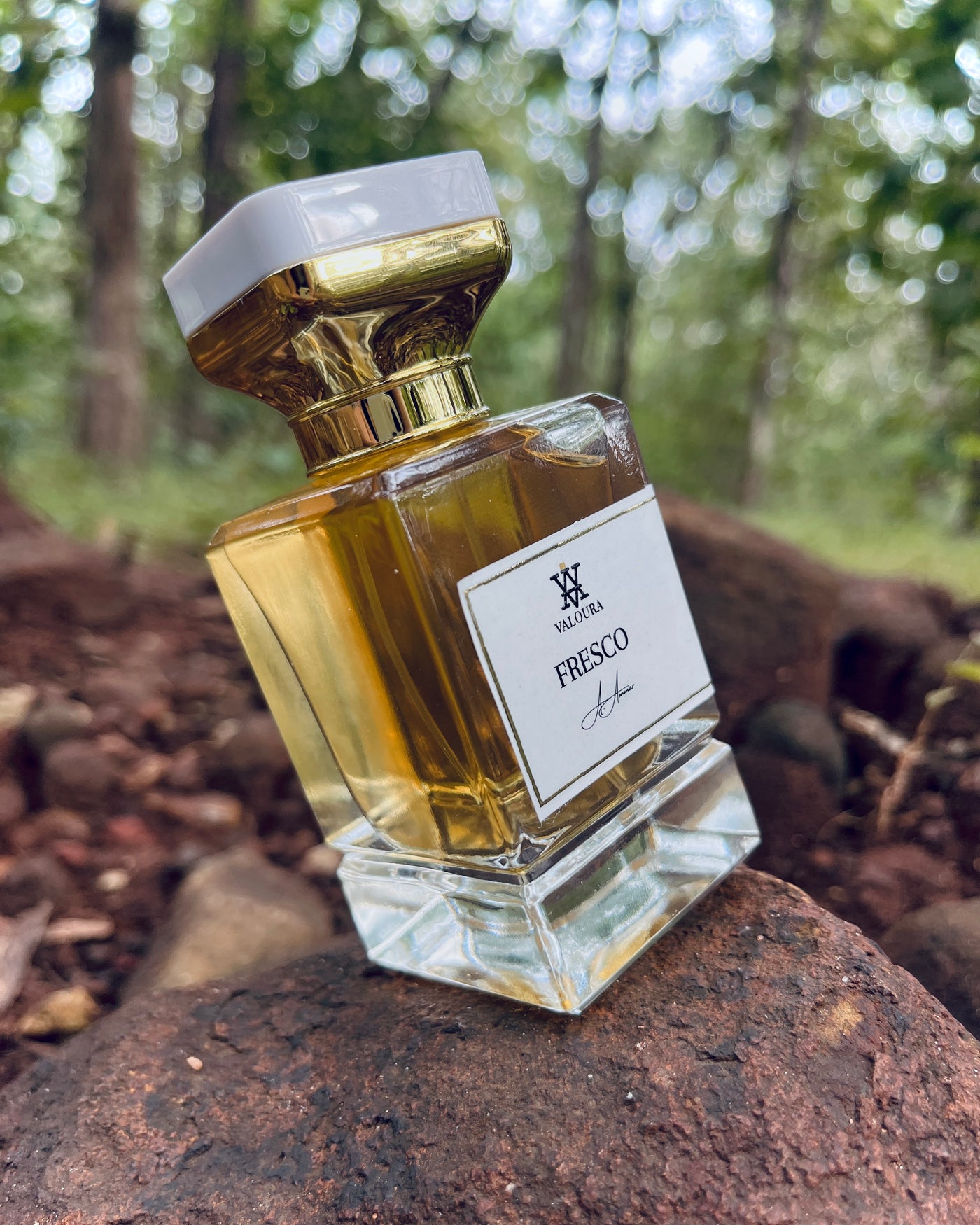 Slanted Perfume bottle labeled 'Fresco' on a rock with a forest background