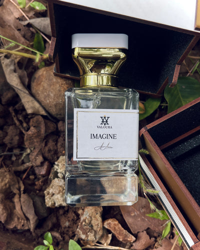 Perfume bottle labeled 'Imagine' by Valoura with box  on a natural background with leaves and rocks.