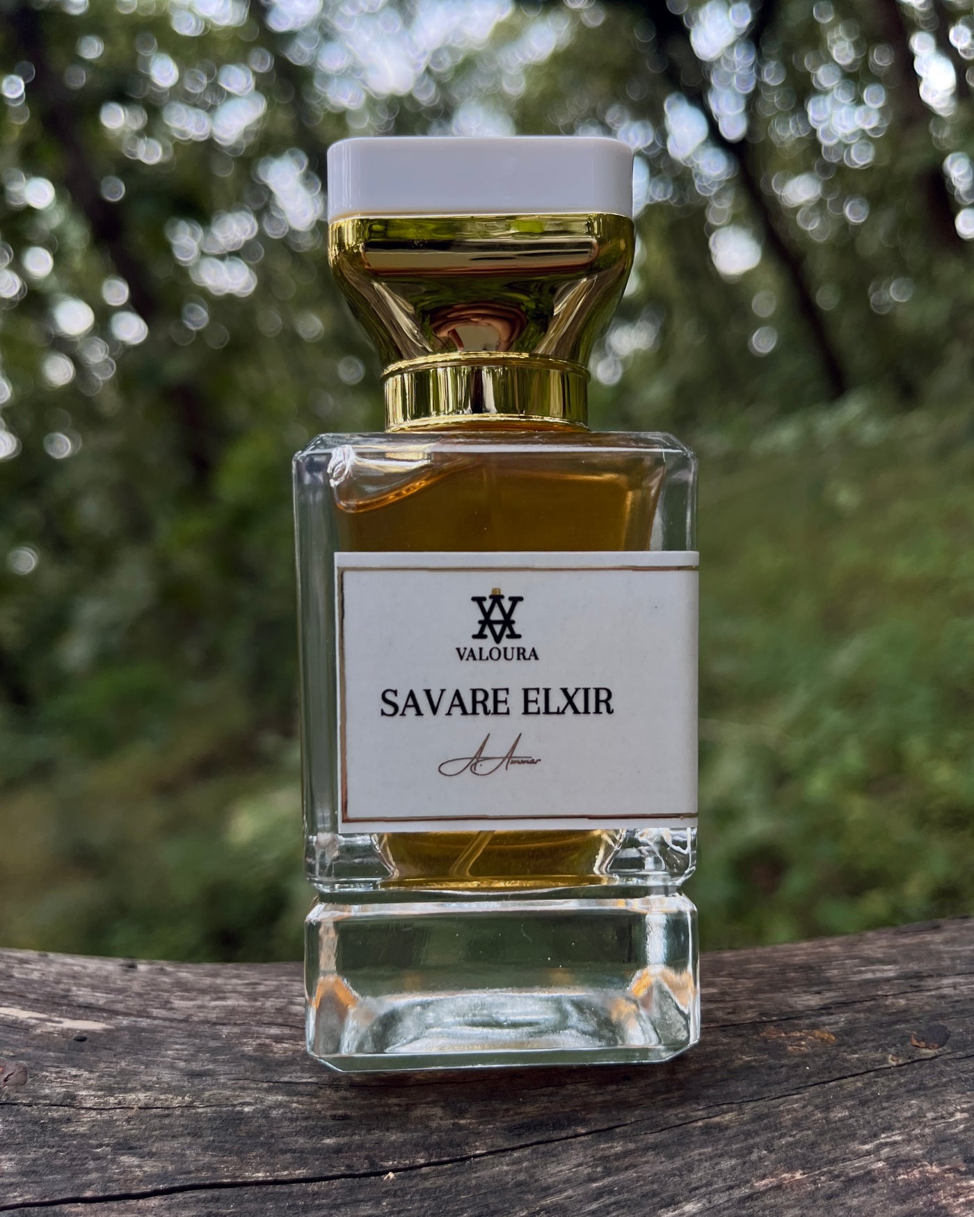 Perfume bottle labeled 'Savare Elixir' by Valoura on a wooden surface with a blurred natural background