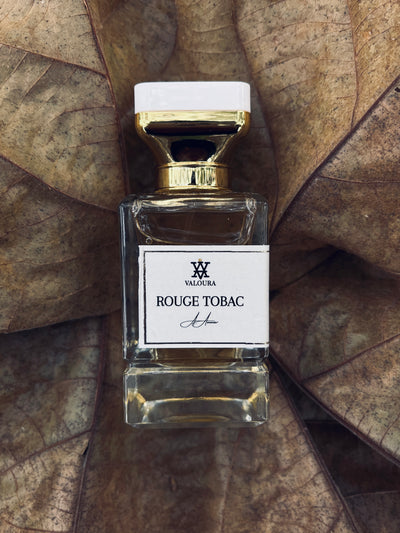Perfume bottle labeled 'Rouge Tabac' by Valoura on a dried Tabaco leafbackground