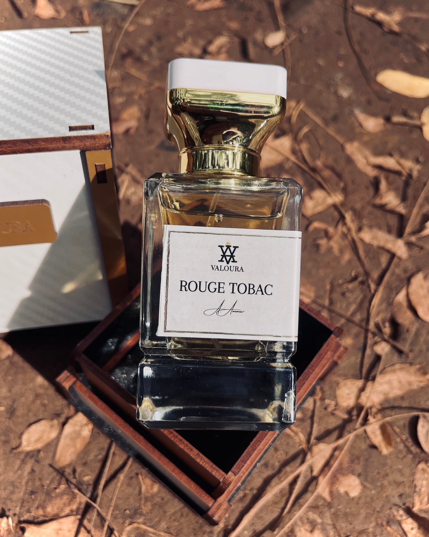 Valoura Rouge Tobac perfume bottle on a wooden packaging box  with leaves and mud 